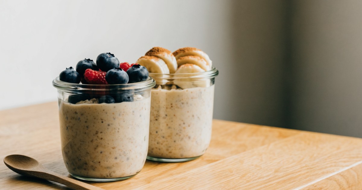 Overnight Oats mit Protein: zwei Gläser mit Beeren und Banane auf einem hellen Holztisch